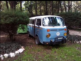 Blue VW van with a tent beside it at a campground under trees in San Cristóbal de las Casas