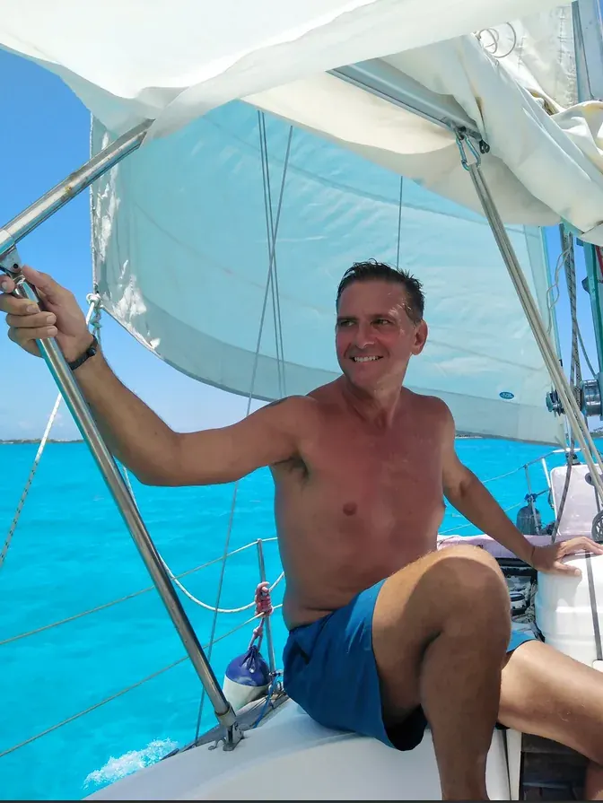 On the sailboat in open water, holding the support pole with turquoise sea behind
