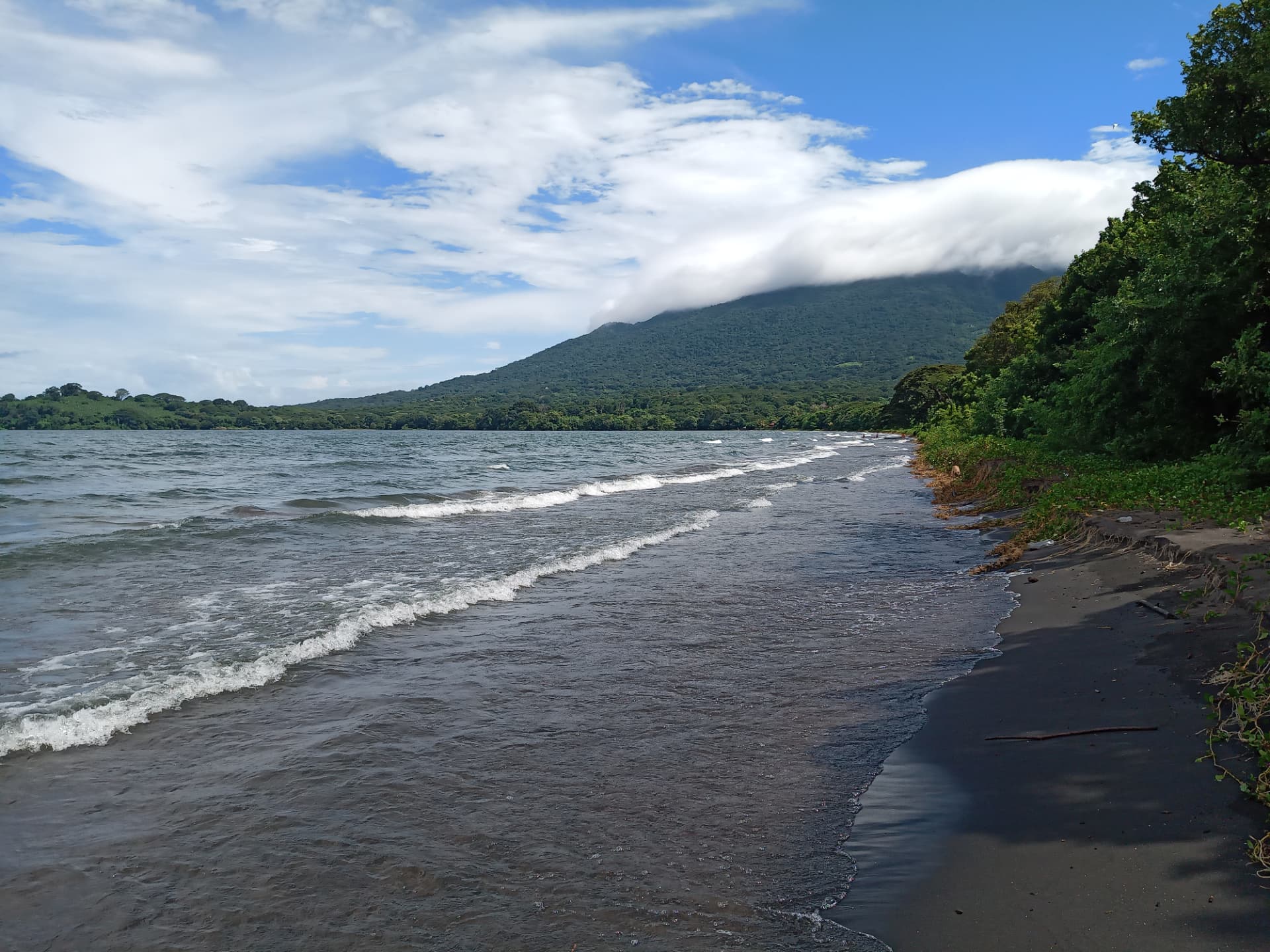 Waves on the shore of Lake Nicaragua with the Maderas volcano rising behind palm-covered hills