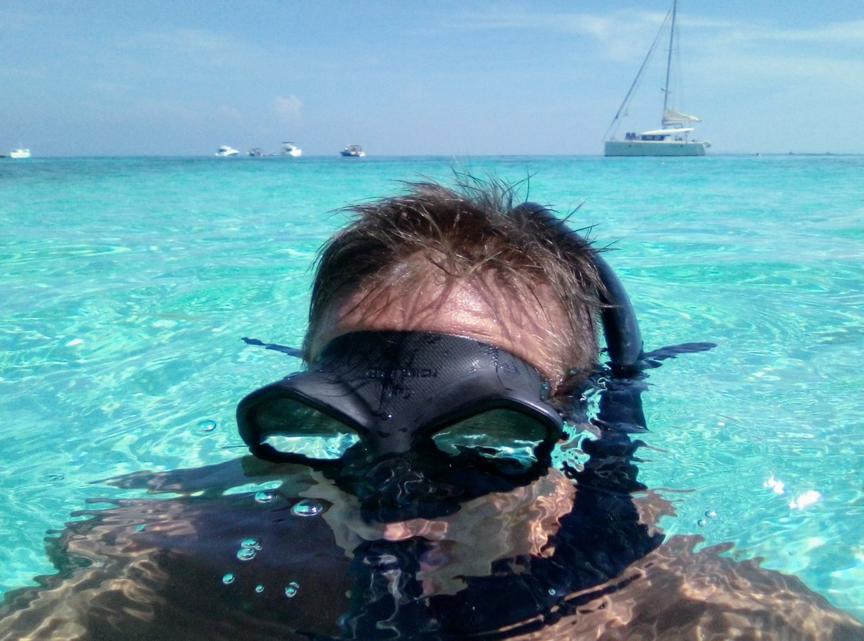 Snorkeling in clear turquoise water off Isla Mujeres with a catamaran in the background
