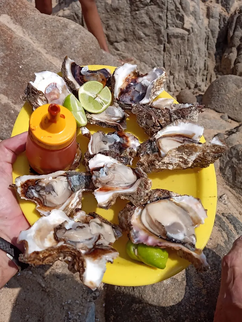 A yellow plate of fresh oysters with lime and hot sauce held on the beach in Puerto Escondido